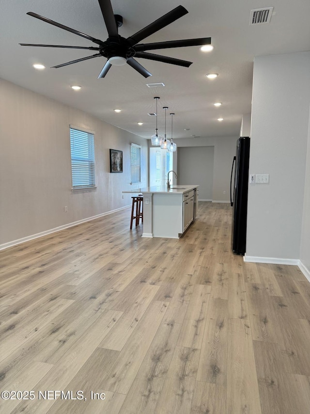 kitchen with a center island with sink, light hardwood / wood-style floors, pendant lighting, black fridge, and sink