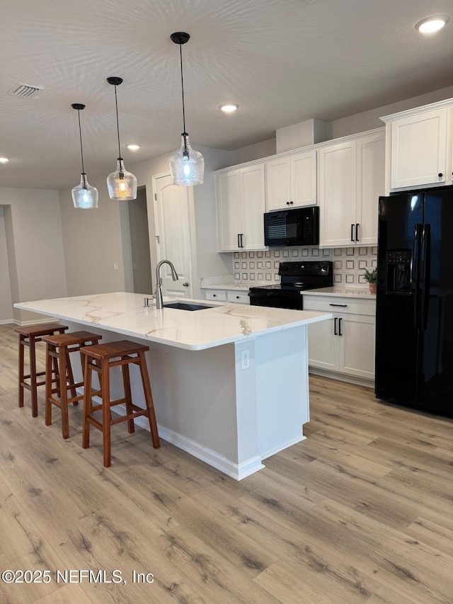 kitchen featuring hanging light fixtures, an island with sink, black appliances, white cabinets, and sink