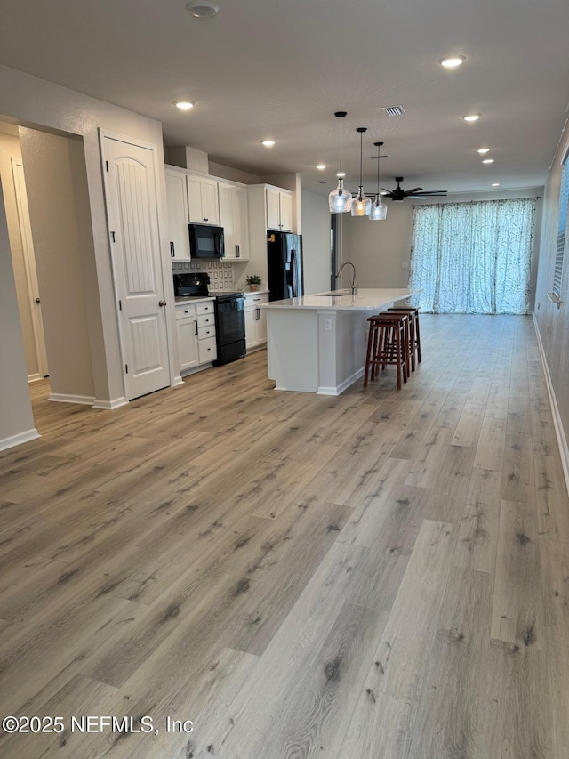 kitchen featuring a center island with sink, black appliances, light hardwood / wood-style floors, pendant lighting, and white cabinets