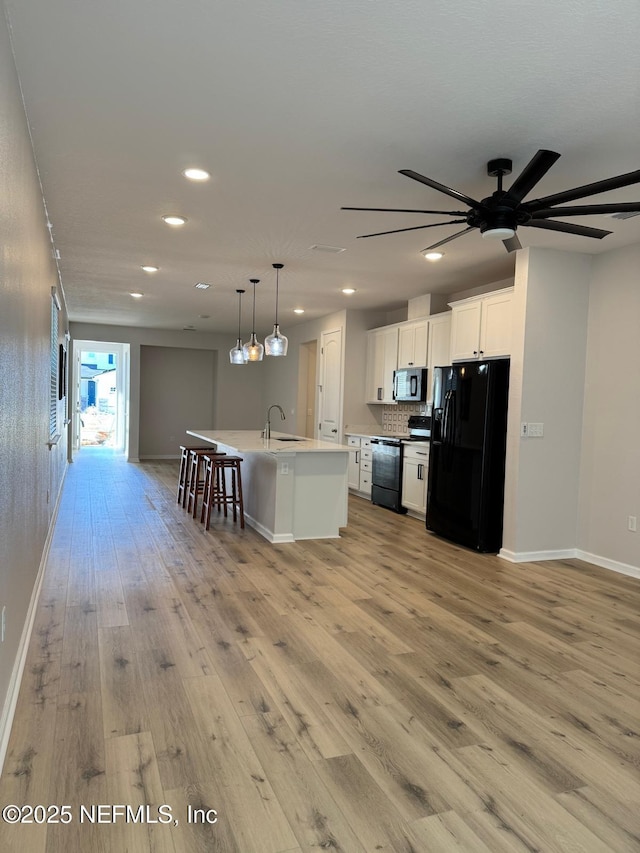 kitchen featuring black appliances, an island with sink, white cabinets, decorative light fixtures, and sink