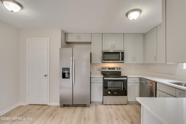 kitchen featuring light wood-type flooring, a textured ceiling, and appliances with stainless steel finishes