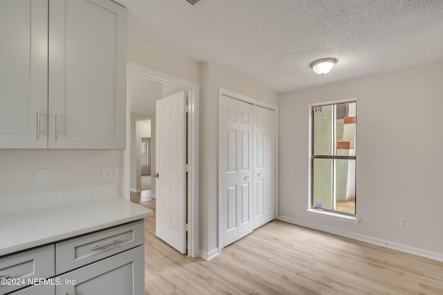 kitchen featuring light stone countertops, a textured ceiling, light hardwood / wood-style floors, and gray cabinets