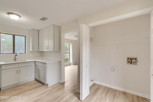 interior space with sink, cabinets, washer hookup, a textured ceiling, and light wood-type flooring