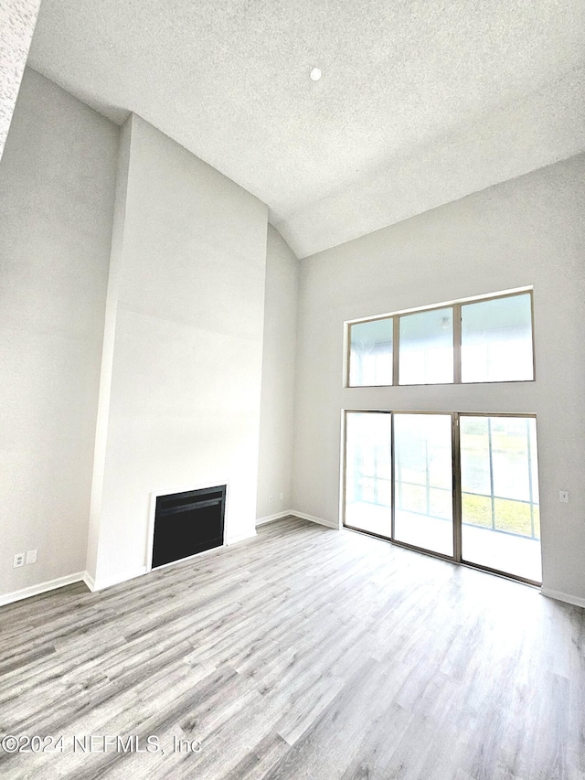 unfurnished living room with a textured ceiling, high vaulted ceiling, and light hardwood / wood-style flooring