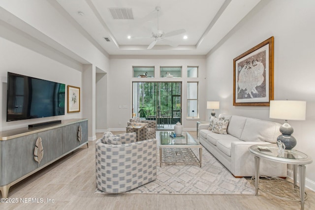 living room with a high ceiling, light hardwood / wood-style floors, ceiling fan, and a tray ceiling