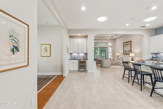 kitchen featuring white cabinetry, a kitchen breakfast bar, wine cooler, backsplash, and light hardwood / wood-style floors