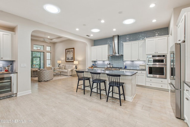 kitchen with a breakfast bar area, white cabinetry, wall chimney exhaust hood, and appliances with stainless steel finishes