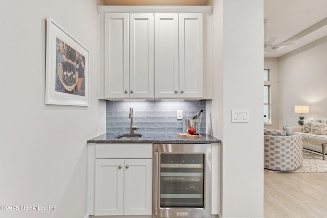 bar with decorative backsplash, white cabinetry, sink, and beverage cooler