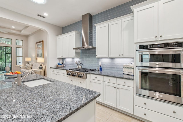 kitchen featuring dark stone counters, white cabinets, sink, wall chimney exhaust hood, and stainless steel appliances