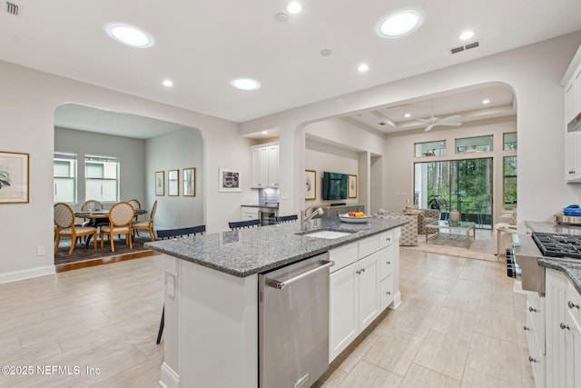 kitchen with white cabinetry, sink, stainless steel dishwasher, dark stone countertops, and a kitchen island with sink