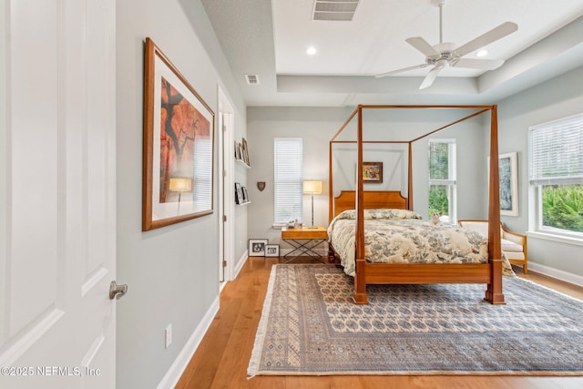 bedroom featuring multiple windows, wood-type flooring, a tray ceiling, and ceiling fan