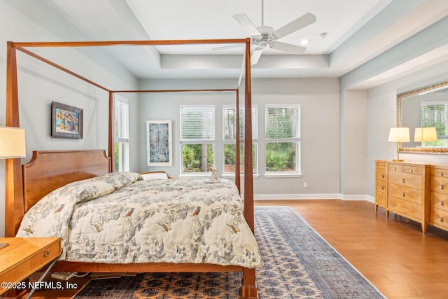 bedroom with ceiling fan, light wood-type flooring, and a tray ceiling