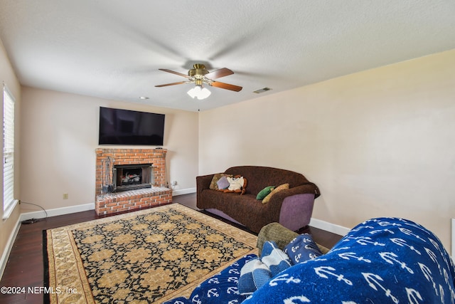 living room with a textured ceiling, ceiling fan, dark hardwood / wood-style flooring, and a fireplace