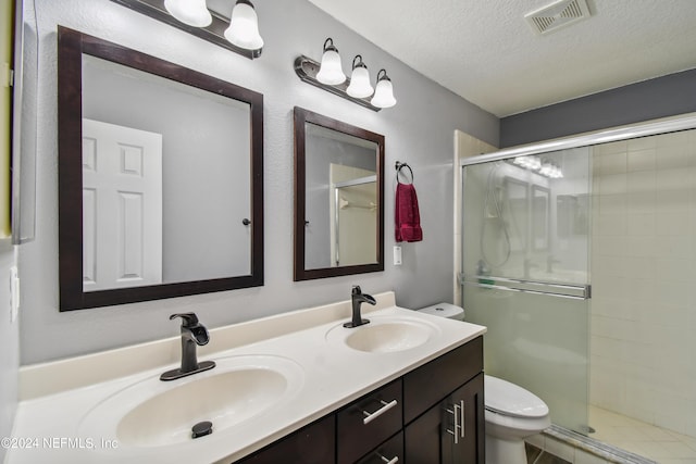 bathroom featuring vanity, toilet, a shower with door, and a textured ceiling