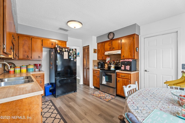 kitchen with sink, a textured ceiling, stainless steel range with electric stovetop, decorative backsplash, and black refrigerator