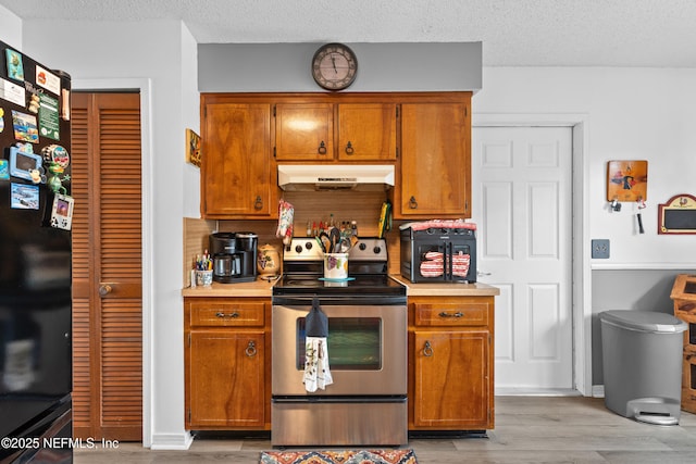 kitchen with black fridge, electric range, a textured ceiling, and light wood-type flooring