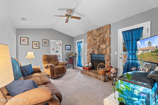 carpeted living room featuring ceiling fan, a stone fireplace, lofted ceiling, and a textured ceiling