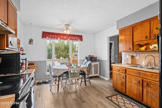 kitchen featuring wall chimney exhaust hood, a textured ceiling, ceiling fan, sink, and light hardwood / wood-style floors