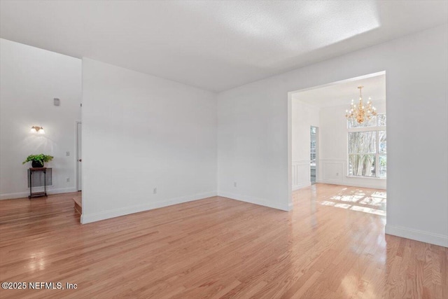 empty room with light hardwood / wood-style floors and an inviting chandelier