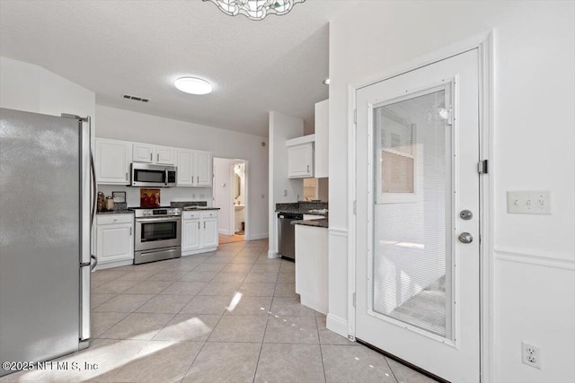 kitchen featuring a textured ceiling, stainless steel appliances, light tile patterned floors, a notable chandelier, and white cabinets