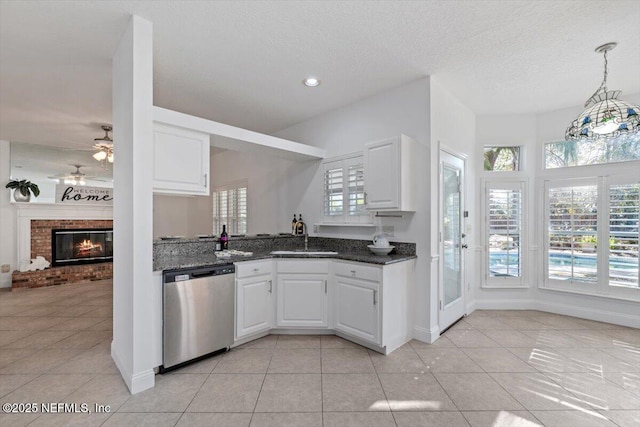 kitchen with white cabinets, sink, stainless steel dishwasher, light tile patterned floors, and a fireplace