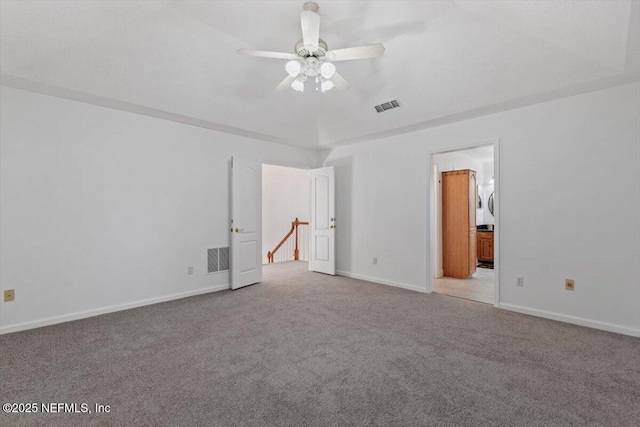 unfurnished bedroom with a raised ceiling, ensuite bath, ceiling fan, and light carpet