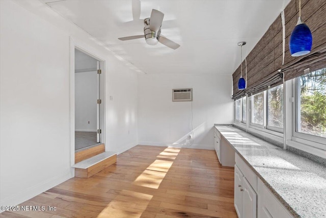 interior space featuring pendant lighting, ceiling fan, a wall mounted AC, light stone counters, and white cabinetry