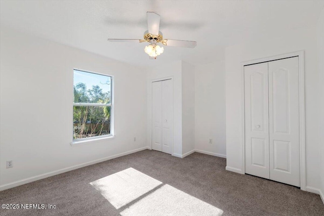 unfurnished bedroom with carpet flooring, ceiling fan, and two closets