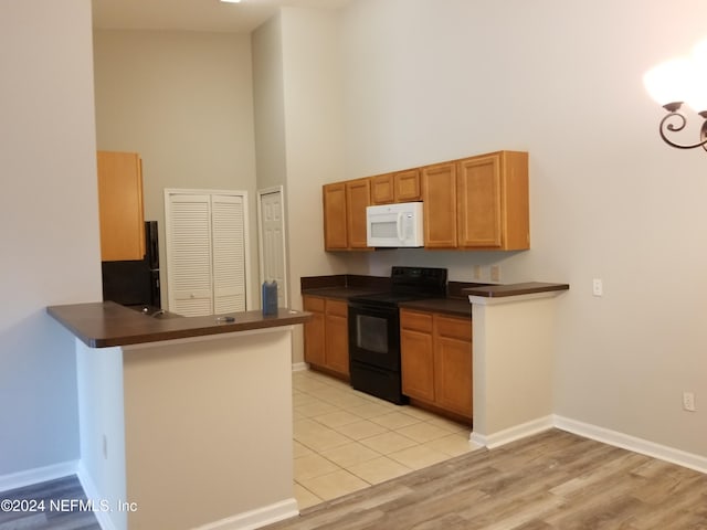 kitchen featuring kitchen peninsula, a high ceiling, light hardwood / wood-style floors, and black appliances