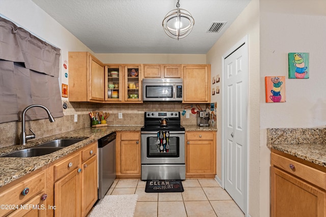 kitchen with appliances with stainless steel finishes, backsplash, light stone counters, sink, and light tile patterned floors