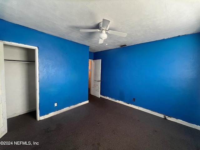 unfurnished bedroom with ceiling fan, dark carpet, and a textured ceiling