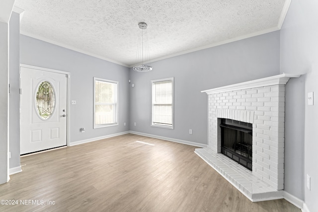 unfurnished living room with light wood-type flooring, ornamental molding, a textured ceiling, a fireplace, and a chandelier