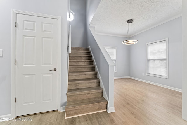 staircase with a chandelier, hardwood / wood-style floors, a textured ceiling, and ornamental molding