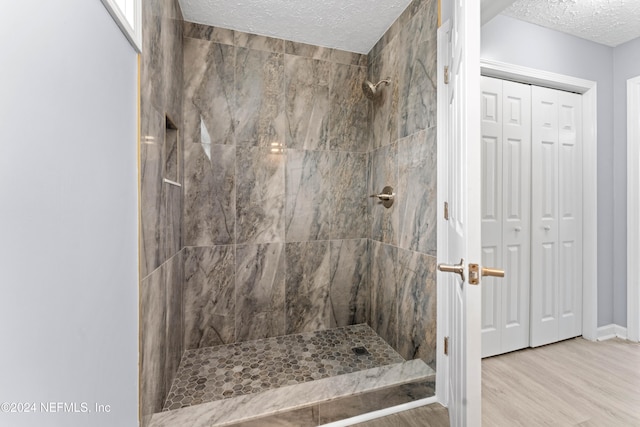 bathroom with a tile shower, a textured ceiling, and wood-type flooring