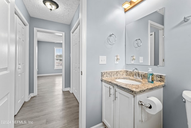 bathroom with hardwood / wood-style floors, vanity, toilet, and a textured ceiling