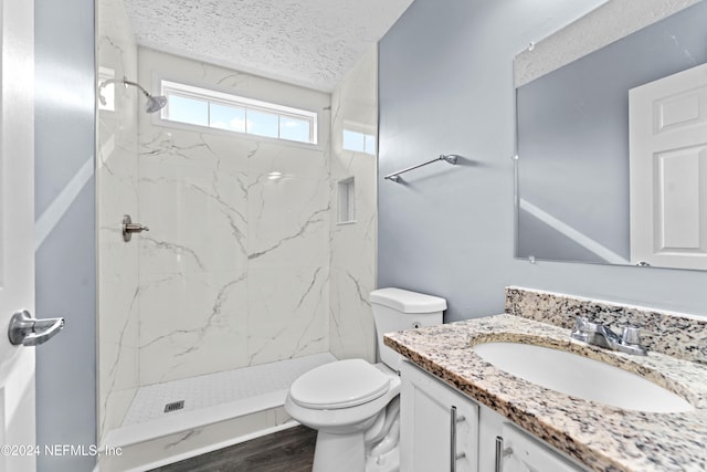 bathroom with a textured ceiling, toilet, tiled shower, vanity, and hardwood / wood-style flooring