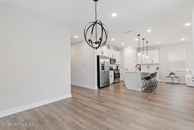 kitchen with stainless steel appliances, pendant lighting, an inviting chandelier, white cabinets, and an island with sink