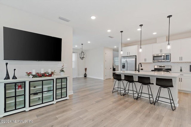 kitchen with stainless steel appliances, light hardwood / wood-style flooring, pendant lighting, a kitchen island with sink, and white cabinets