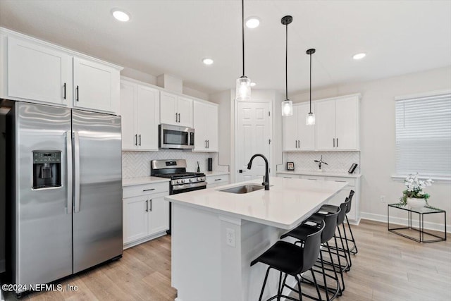 kitchen featuring stainless steel appliances, a kitchen island with sink, sink, pendant lighting, and white cabinetry