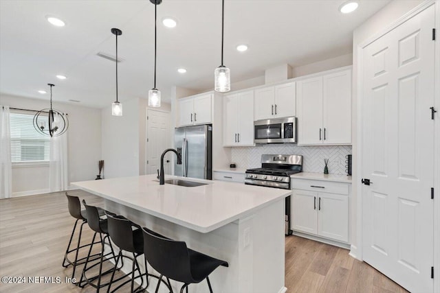 kitchen featuring decorative light fixtures, white cabinetry, an island with sink, and appliances with stainless steel finishes