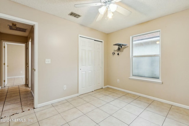 unfurnished bedroom with ceiling fan, light tile patterned floors, a textured ceiling, and a closet