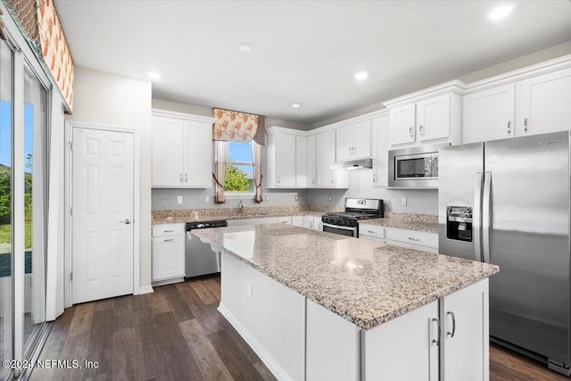 kitchen with white cabinets, stainless steel appliances, a kitchen island, and light stone countertops