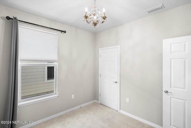 carpeted spare room with a textured ceiling and an inviting chandelier