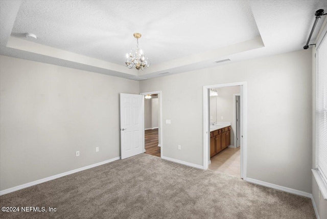 unfurnished bedroom featuring a raised ceiling, light colored carpet, connected bathroom, and an inviting chandelier