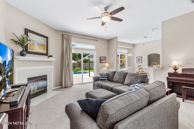 living room with ceiling fan, a fireplace, light colored carpet, and a textured ceiling