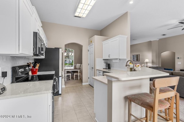 kitchen featuring kitchen peninsula, appliances with stainless steel finishes, a kitchen breakfast bar, white cabinets, and light tile patterned flooring