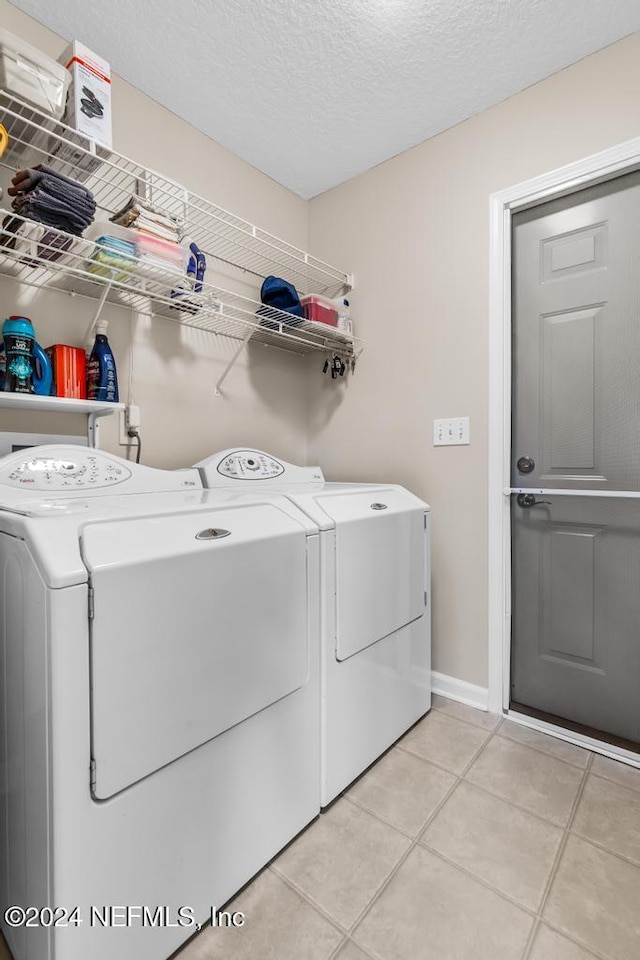 washroom with light tile patterned flooring, washer and dryer, and a textured ceiling