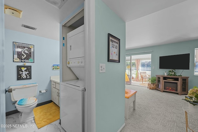 clothes washing area featuring light colored carpet and stacked washer / dryer