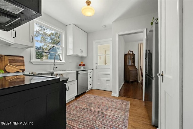 kitchen featuring exhaust hood, white cabinets, sink, light hardwood / wood-style flooring, and stainless steel dishwasher