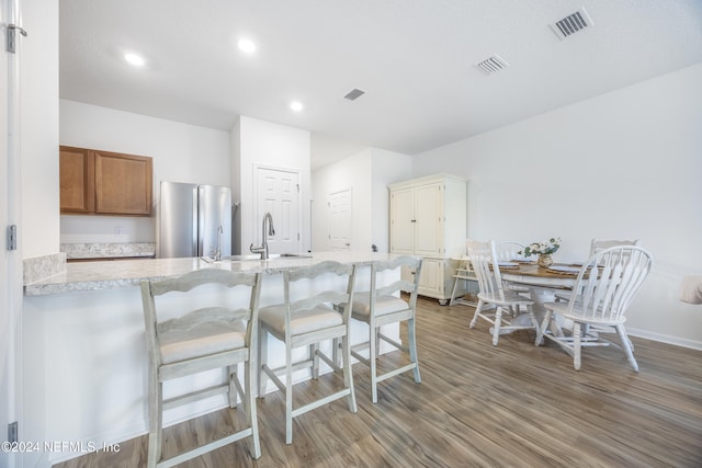 kitchen with sink, kitchen peninsula, stainless steel fridge, a breakfast bar area, and light wood-type flooring